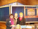 Three women sitting at a news desk on a TV show set.