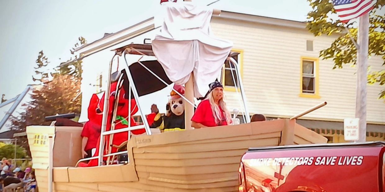 People in costumes on a boat float during a parade near a red truck.