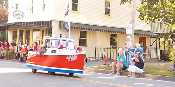 A small boat float drives down a street in a parade with spectators watching.