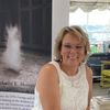 Smiling woman in white dress sitting indoors near a window and display.