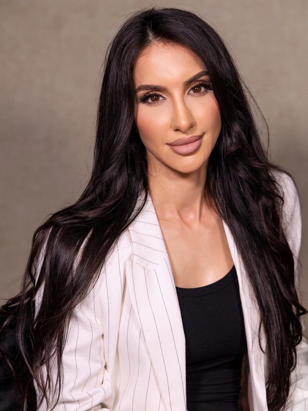 Portrait of a confident woman with long dark hair in a white blazer and black top.