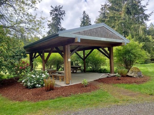 Wooden pavilion with picnic tables in a green park.