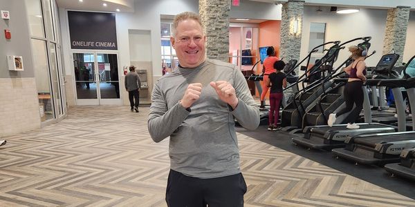 A man smiling and posing in a gym near treadmills.