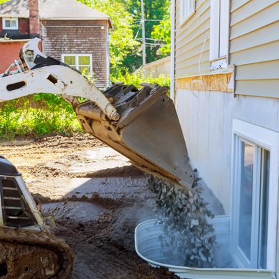 Excavator filling basement window well with gravel.