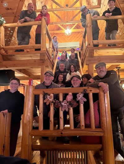 A large family gathers on a wooden staircase inside a cozy cabin.