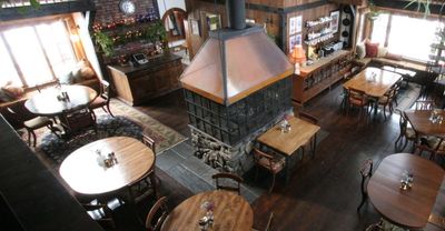 Cozy rustic restaurant interior with wooden tables and a central fireplace.