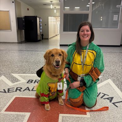 A woman and dog in matching Ninja Turtle costumes at a hospital.