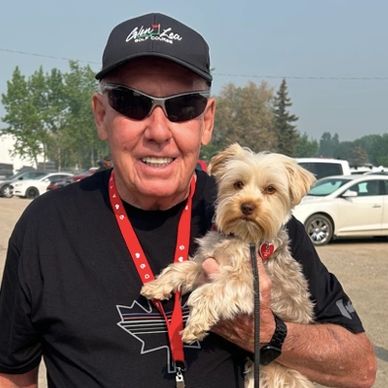 Smiling man in sunglasses holding a small dog outdoors.