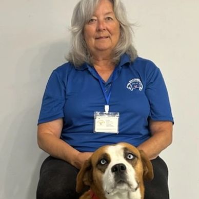 Woman in blue shirt sitting with a brown and white dog with blue eyes.