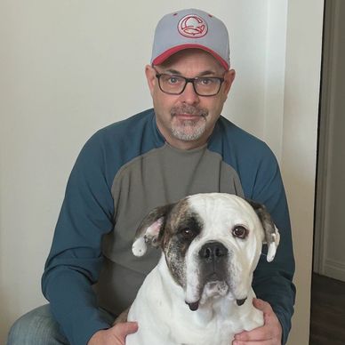 Man wearing glasses and cap with a large white and brown dog.
