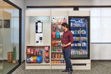 Man shopping at a modern, automated office snack station with various snacks and beverages.