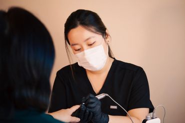 A masked nail technician carefully works on a client's nails.