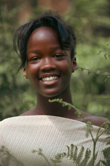 Smiling woman in a white textured top surrounded by greenery.