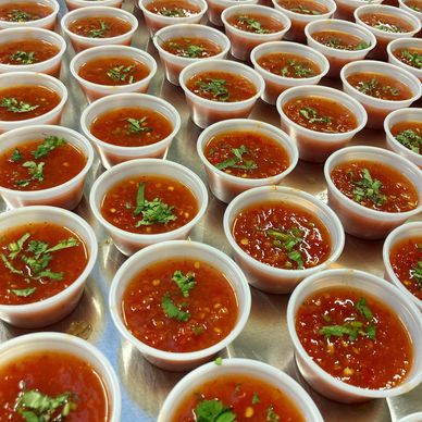 Multiple small cups filled with red sauce garnished with chopped herbs.