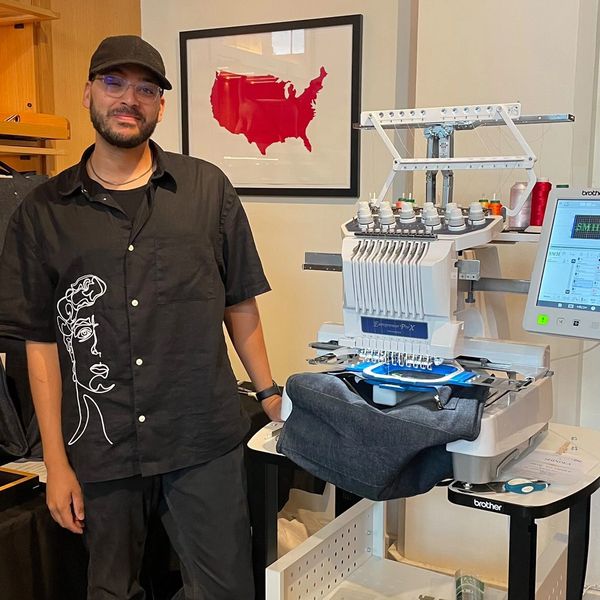 Evan is standing next to the embroidery machine in a store.