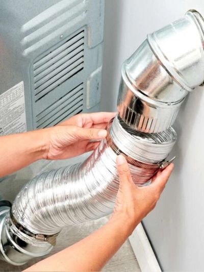 Hands installing a flexible silver duct pipe on a metal vent.