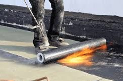 Worker applying torch-on roofing membrane with flame.