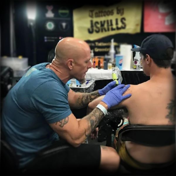 Tattoo artist focused while tattooing a client's shoulder at a studio.
