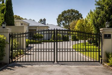 Elegant black metal gates at a large house entrance.