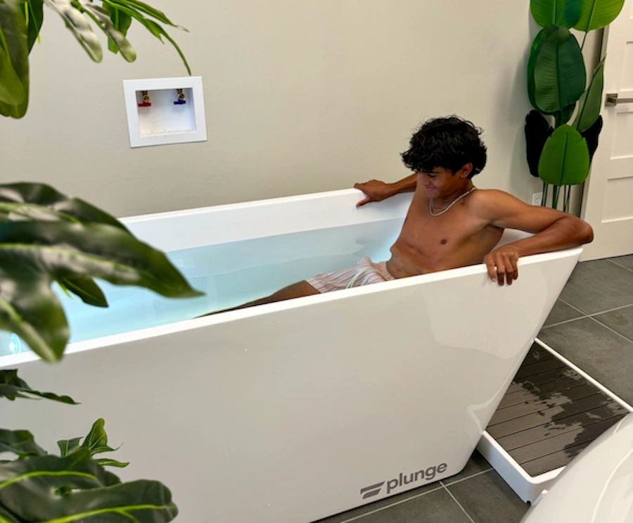 A young man relaxing in a modern white cold plunge tub indoors with plants around.