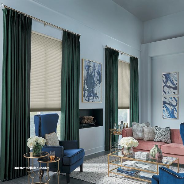 Elegant living room with deep green curtains, beige cellular shades, and a mix of blue and pink furniture.