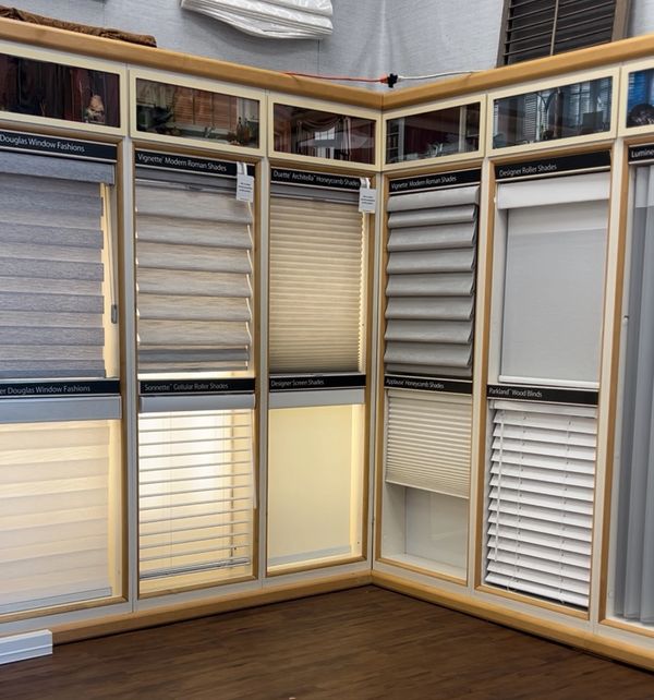 Display of various window shades and blinds in a showroom corner.