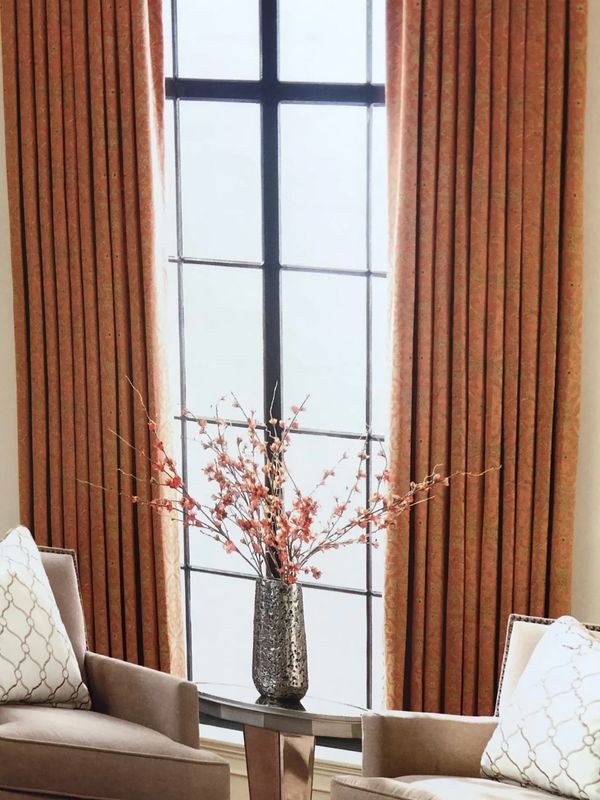 Elegant living room corner with floral arrangement and beige armchairs by a large window.