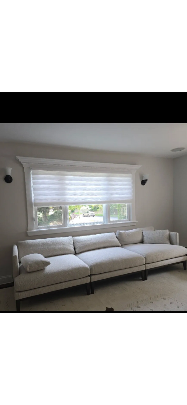Modern beige sectional sofa under a large window with white blinds.