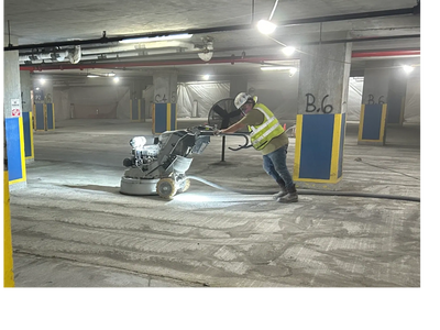 Worker using a floor grinding machine in a parking garage.