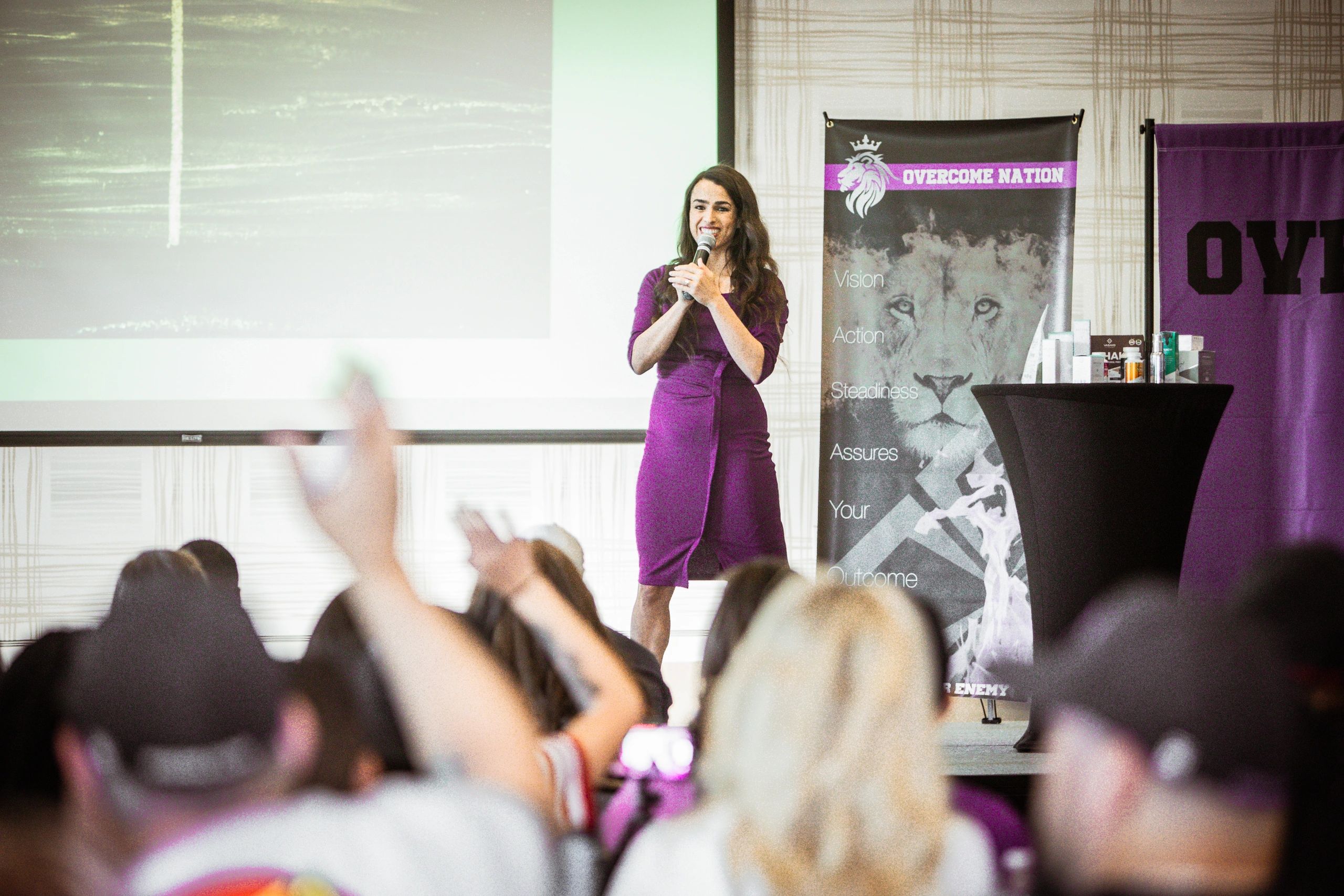 Woman speaking at a conference with audience hands raised.