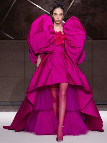 Model in vibrant pink high-low dress with large sleeves.