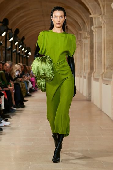 Model walks runway in vibrant green dress with black gloves and boots.