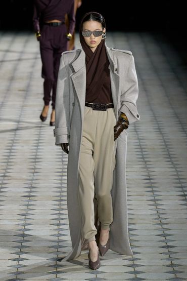 Model showcases a chic winter outfit with a long gray coat and beige pants.