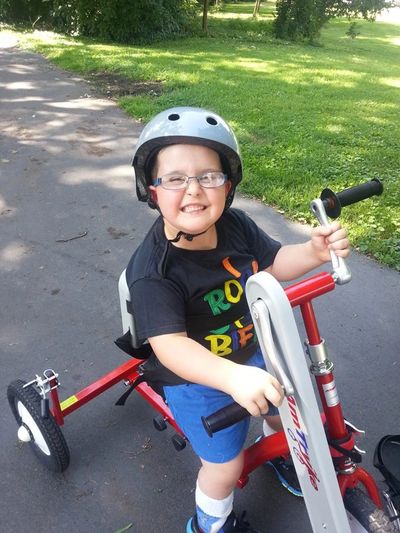 Child smiling on a red tricycle wearing a helmet.
