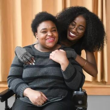 Two joyful women sharing a warm embrace, one in a wheelchair.