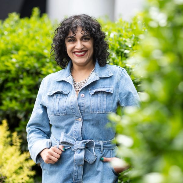 Woman in a denim jacket smiling outdoors.