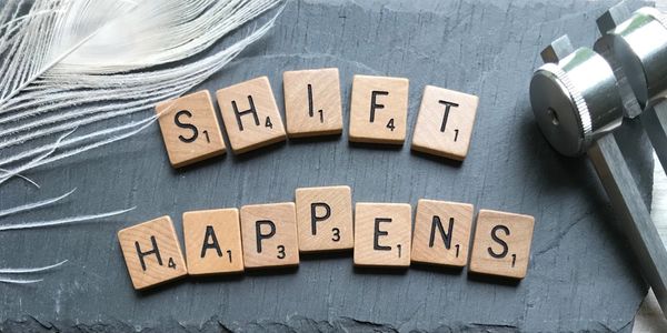 Scrabble tiles spell 'SHIFT HAPPENS' on a slate surface.