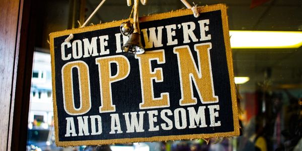 Sign saying "Come in we're open and awesome" hanging on a door.