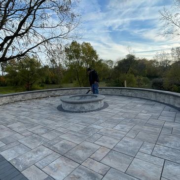  circular stone patio with a fire pit in the center and surrounded by trees