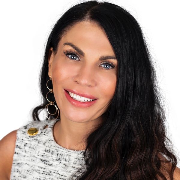 Smiling woman with long dark hair and blue eyes wearing hoop earrings and a textured top.
