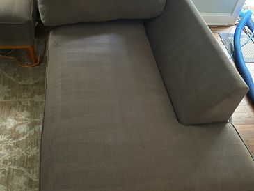Brown sectional sofa with wooden legs on a patterned rug.