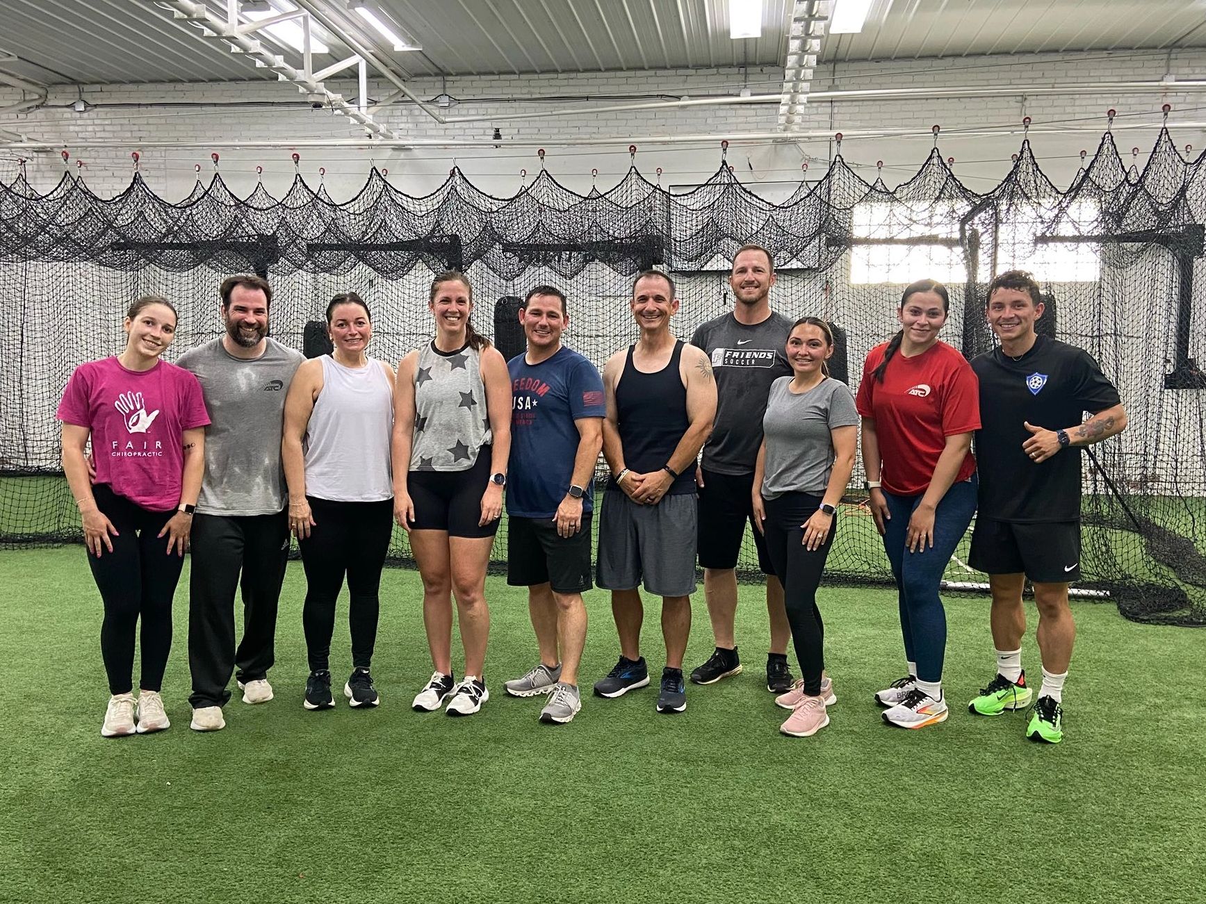 A group of ten people posing together inside a sports facility with netting in the background.