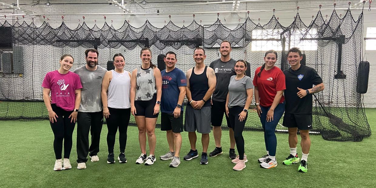 A group of ten people posing together inside a sports facility with netting in the background.