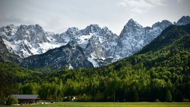 Snow-capped mountains with lush green forest and a small cabin in the valley.