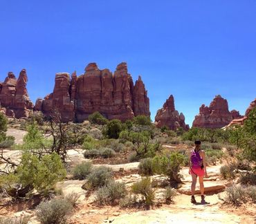 A woman hiking in a desert with red rock formations under a clear blue sky.
