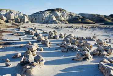 Rock formations casting long shadows in a desert landscape under a clear sky.