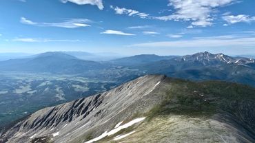 Expansive mountain range under a bright blue sky with scattered clouds.