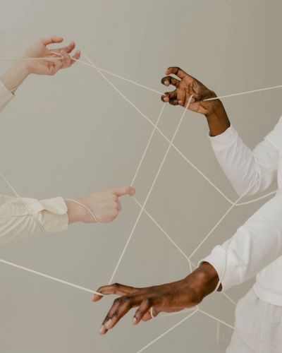 Hands of diverse people connected by intertwined white strings.