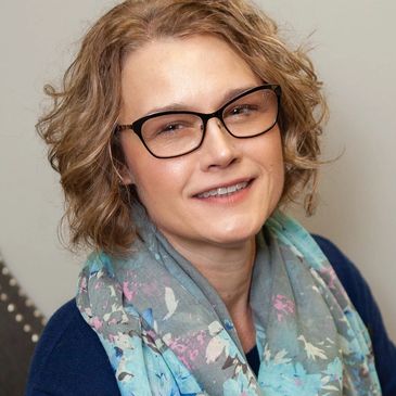 Smiling woman wearing glasses and a patterned scarf.