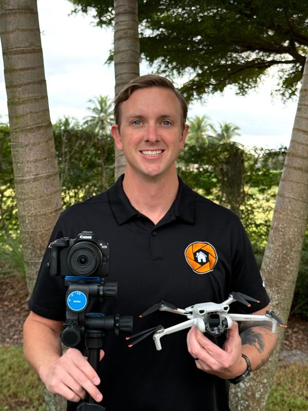 Man holding a camera on a tripod and a drone outdoors.
